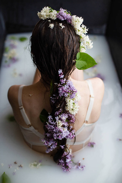 Beautiful young woman in milk bath, spa and skincare concept. Brunette girl relaxing in milk floral bath, back view - Fotografie, Obrázek