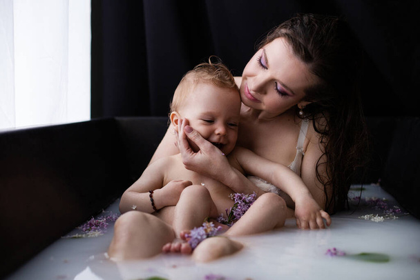 Nuori onnellinen äiti poikavauvan kanssa kukkamaitokylvyssä. Äiti ja lapsi tarjouksen halaus kylvyssä - Valokuva, kuva