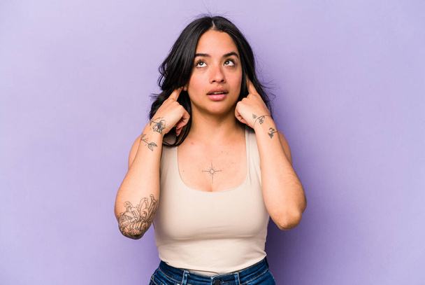Young hispanic woman isolated on purple background covering ears with fingers, stressed and desperate by a loudly ambient. - Photo, Image