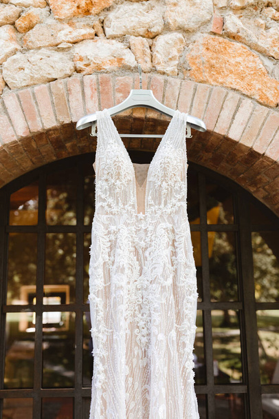 Beautiful bride's dress hanging on a hanger near the wall. Preparation for the ceremony - Foto, Imagen