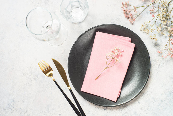 Table minimaliste avec assiette noire, fleurs et couverts sur fond blanc. Vue de dessus avec espace pour le design. - Photo, image