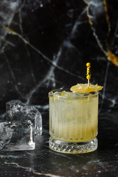 Alcoholic Scotch Whiskey Penicillin Drink Cocktail with Lemon, Honey syrup and Candied Ginger. Cocktail glass on black background. - Photo, Image
