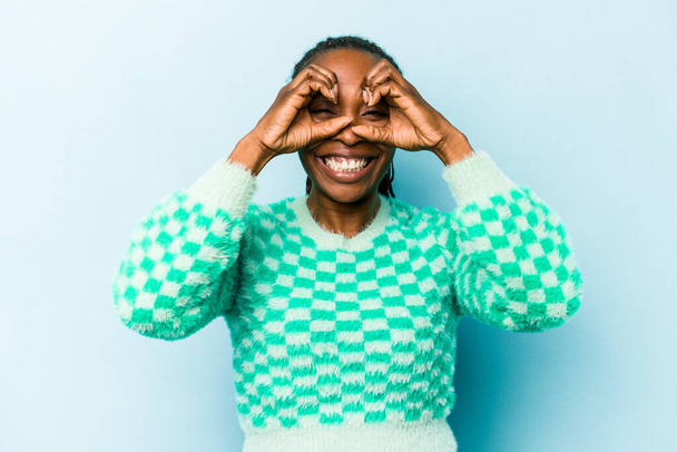 Young african american woman isolated on blue background showing okay sign over eyes - Foto, immagini