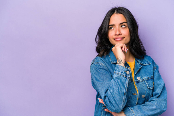 Young hispanic woman isolated on purple background looking sideways with doubtful and skeptical expression. - Photo, Image