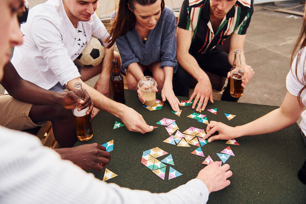Playing card game. Group of young people in casual clothes have a party at rooftop together at daytime. - Valokuva, kuva