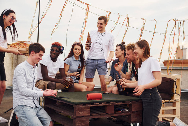 With delicious pizza. Group of young people in casual clothes have a party at rooftop together at daytime. - Foto, afbeelding