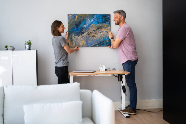Happy Couple Hanging Painting. Wall Decoration At Home - 写真・画像