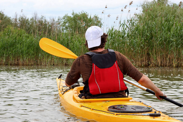 Rear view of kayaker man paddle yellow kayak on Danube river. Summer kayaking. Concept for adventure, travel, action, lifestyle - Foto, imagen