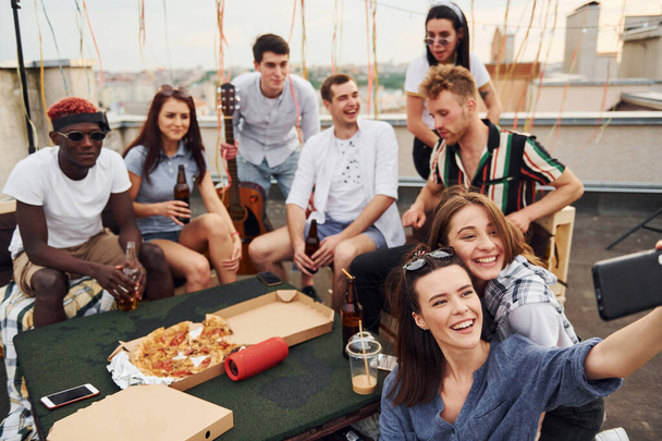 Girl making selfie. With delicious pizza. Group of young people in casual clothes have a party at rooftop together at daytime. - Fotó, kép