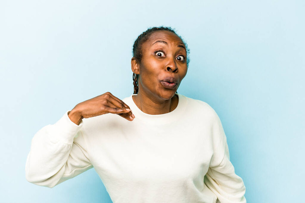 Junge afrikanisch-amerikanische Frau isoliert auf blauem Hintergrund über etwas lachend, Mund mit Händen bedeckt. - Foto, Bild