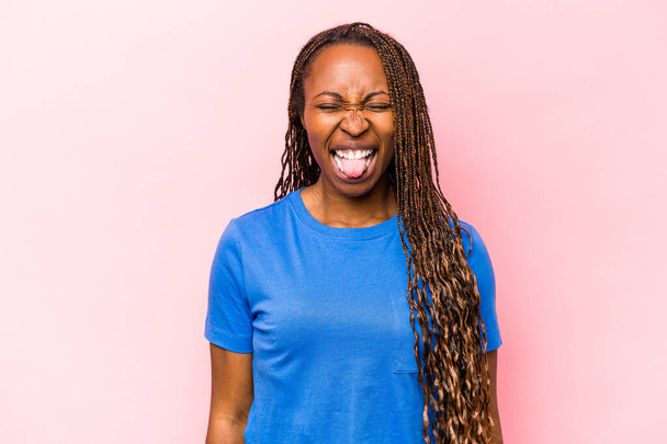 Молода афроамериканська жінка, ізольована на рожевому фоні, смішна й привітна, що вирізняє язик.. - Фото, зображення