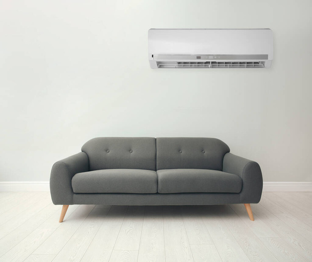 Modern air conditioner on white wall in room with stylish grey sofa - Fotó, kép