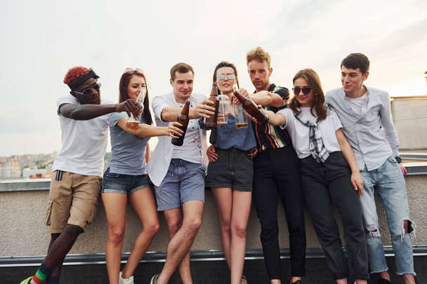 Standing with alcohol at the edge of rooftop. Group of young people in casual clothes have a party together at daytime. - Photo, image