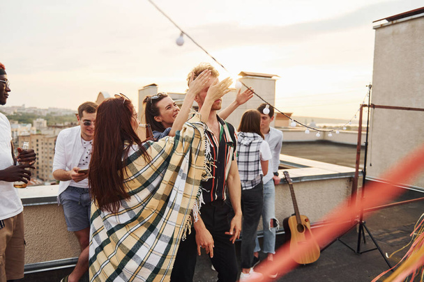 Playing game. Man's eyes covered by hands. Group of young people in casual clothes have a party at rooftop together at daytime. - Foto, Imagem