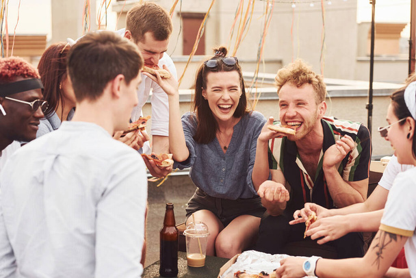 Delicious pizza. Group of young people in casual clothes have a party at rooftop together at daytime. - Foto, imagen