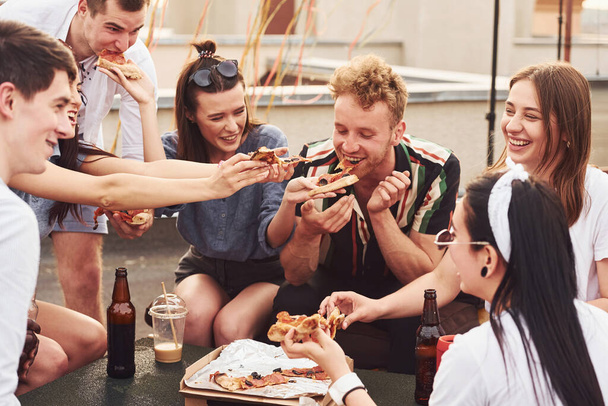 Delicious pizza. Group of young people in casual clothes have a party at rooftop together at daytime. - Foto, Imagen