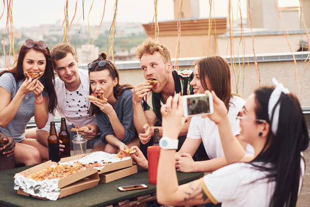 Making photo. Delicious pizza. Group of young people in casual clothes have a party at rooftop together at daytime. - Foto, Imagem
