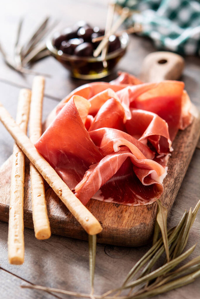 Spanish serrano ham with olives and breadstick on wooden table - Photo, Image