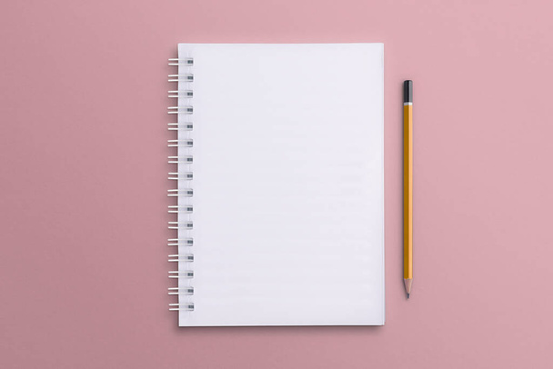 Egy fehér jegyzetfüzet és ceruza kerül egy rózsaszín papír felületre. Jegyzetfüzet. - Fotó, kép