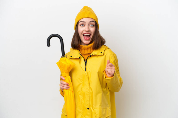 Молода українська жінка з дощовитим пальто і парасолька ізольована на білому тлі, відзначаючи перемогу в положенні переможця. - Фото, зображення