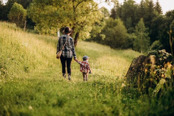 Aktív életmód egy gyermekkel rendelkező anyától. Sétálj ki a szabadba nyáron. Nyári kirándulás gyerekekkel a hegyekbe. Esti séta egy gyermekkel egy alpesi faluban nyáron.. - Fotó, kép