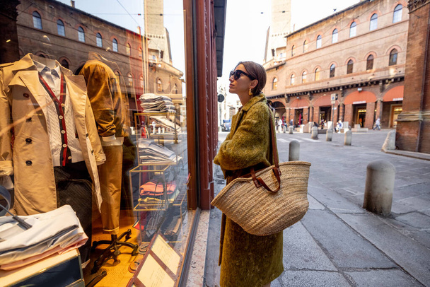 Женщина возле витрины магазина с роскошной одеждой на улице в Болонье - Фото, изображение