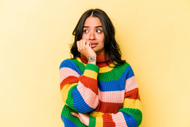 Junge hispanische Frau isoliert auf gelbem Hintergrund beißt Fingernägel, nervös und sehr ängstlich. - Foto, Bild