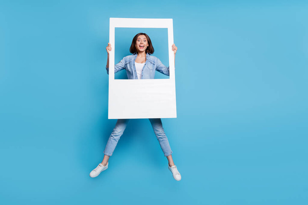 Photo of sweet excited lady dressed denim shirt jumping high holding photo border isolated blue color background - Φωτογραφία, εικόνα