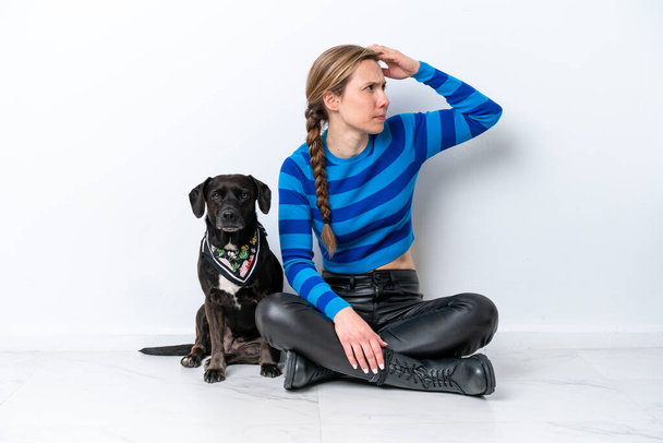 Young caucasian woman sitting on the floor with his puppy isolated on white background having doubts and with confuse face expression - Foto, Imagem