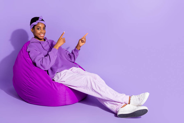Full body photo of nonbinary person sit armchair promote product bargains recommendation isolated on violet color background - 写真・画像