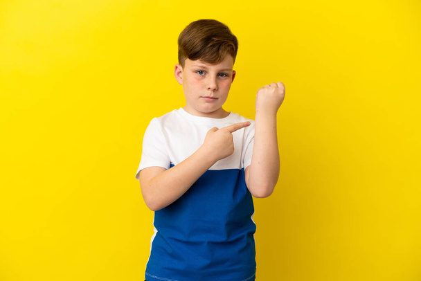 Little redhead boy isolated on yellow background making the gesture of being late - Фото, зображення