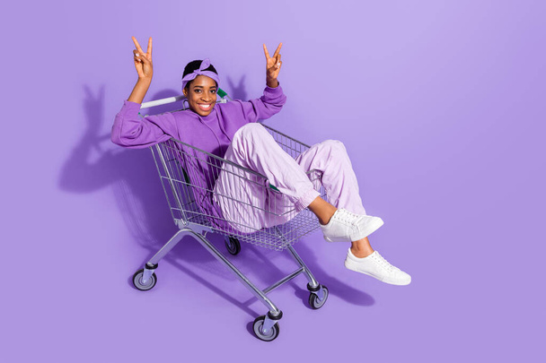 Photo of cheerful friendly transgender person sit cart show v-sign wear headband hoodie isolated violet color background - Фото, изображение
