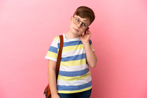 Little redhead caucasian boy isolated on pink background having doubts - Foto, afbeelding