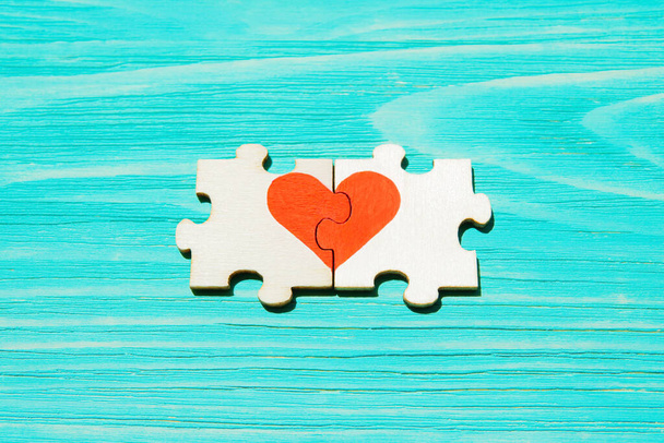 Heart symbol made from two wooden jigsaw puzzle pieces on a blue wooden background. Matching souls concept. - 写真・画像