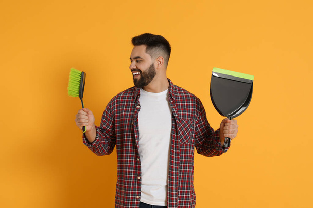 Young man with broom and dustpan on orange background - Photo, image