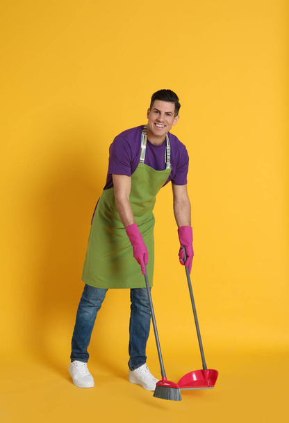 Man with broom and dustpan on orange background - Фото, изображение