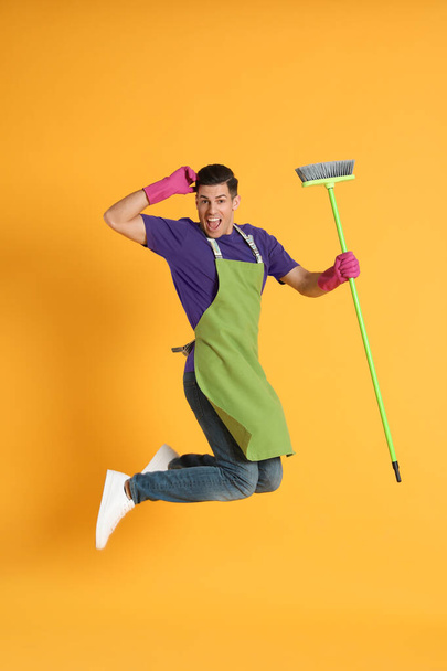 Man with green broom jumping on orange background - Foto, imagen