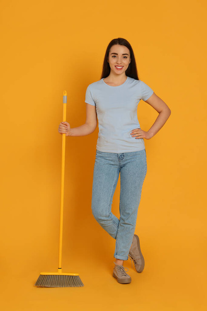 Beautiful young woman with broom on yellow background - Fotoğraf, Görsel