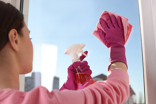 Young woman cleaning window glass with rag and detergent at home - Photo, image