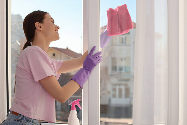Jovem mulher limpeza janela de vidro com pano em casa - Foto, Imagem