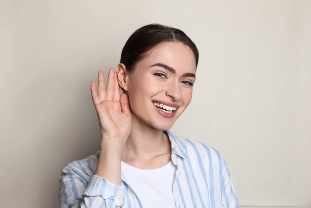 Mladá žena ukazující gesto ruky k uchu na světlém pozadí - Fotografie, Obrázek