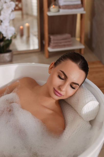 Young woman using pillow while enjoying bubble bath indoors - Foto, Imagen