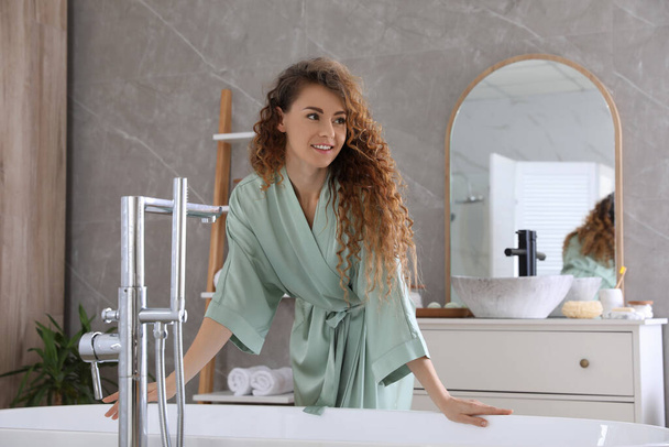 Beautiful woman in green silk robe near bathtub at home - Фото, зображення