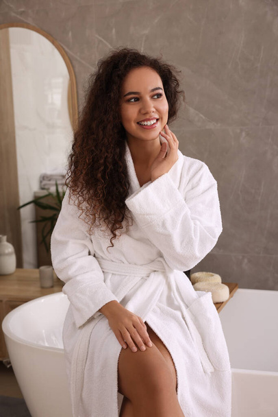Beautiful African American woman sitting on edge of tub in bathroom - Valokuva, kuva