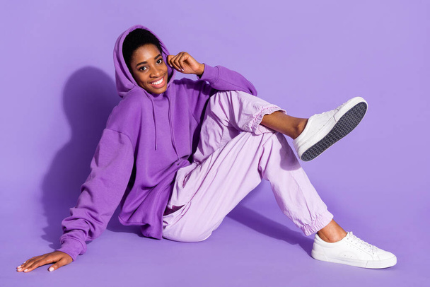 Full length photo of nice young lady sit wear hoodie trousers sneakers isolated on purple color background - Foto, imagen