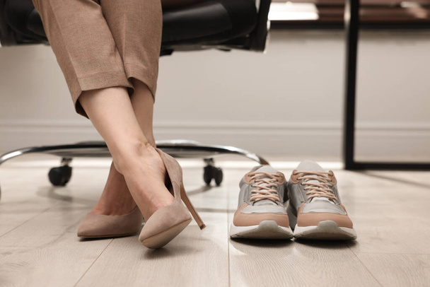 Comfortable sneakers on floor near woman wearing stylish high heeled shoes in office, closeup - Valokuva, kuva
