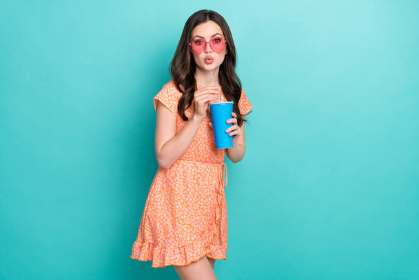 Zdjęcie marzycielskiej dziewczyny nosić pomarańczowy strój usłyszeć okulary pić napój odizolowany turkusowy kolor tła - Zdjęcie, obraz