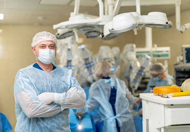 Professional surgeon in blue uniform and protective face mask. Portrait of doctor in glasses standing in operating room. - Фото, зображення