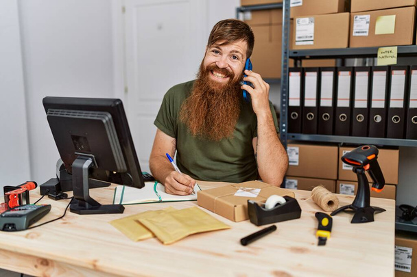 Genç kızıl saçlı iş adamı ofisteki akıllı telefondan konuşuyor. - Fotoğraf, Görsel