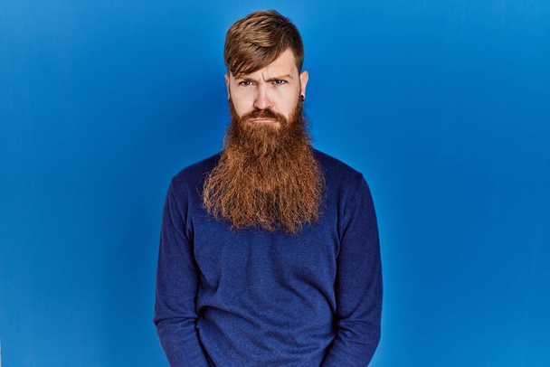 Redhead man with long beard wearing casual blue sweater over blue background skeptic and nervous, frowning upset because of problem. negative person.  - Фото, зображення